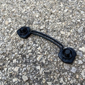 May include: A black plastic cable tie with a rounded end and a small hole. The tie is designed to secure cables and wires.