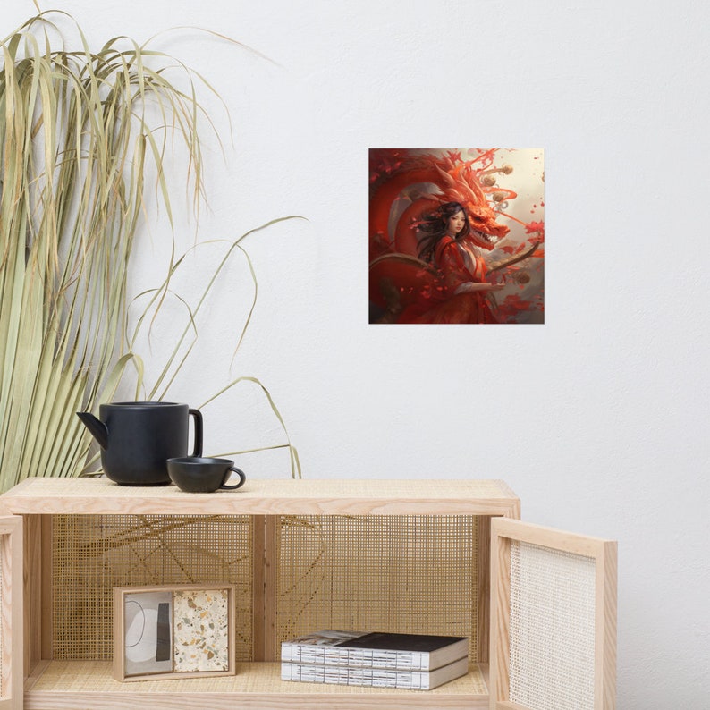 May include: A framed art print depicting a woman in a red dress and a red dragon. The artwork has a fantasy theme with a detailed illustration style. The dragon is behind the woman, with red and orange tones dominating the colour palette.