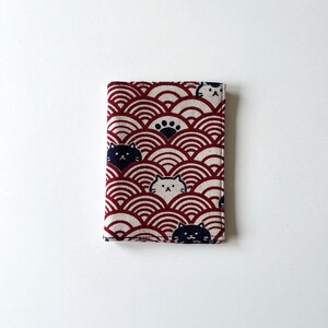 May include: A red and white fabric wallet with a pattern of overlapping circles and cats. The cats are black and white and have different expressions.