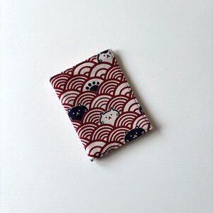 May include: A red and white fabric wallet with a pattern of black cats and white cats on a red and white wave design.