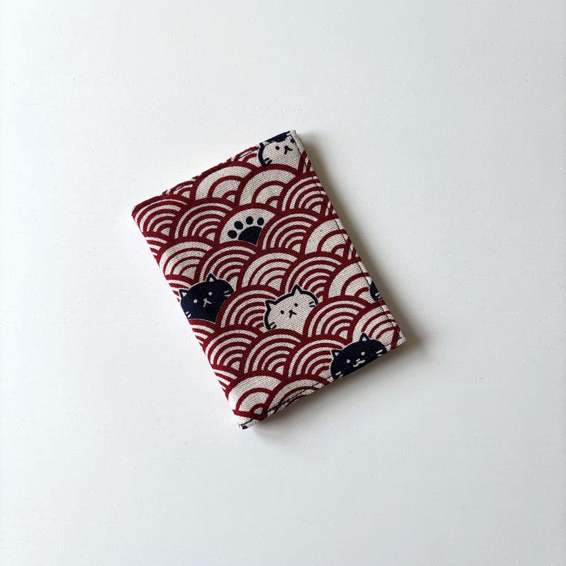 May include: A red and white fabric wallet with a pattern of black cats and white cats on a red and white wave design.