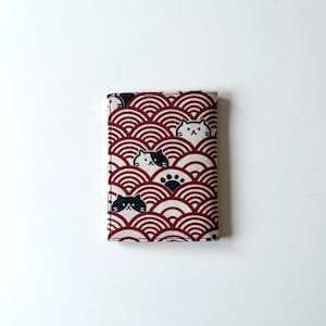 May include: A red and white fabric wallet with a pattern of black and white cats and paw prints. The fabric has a wave-like pattern.
