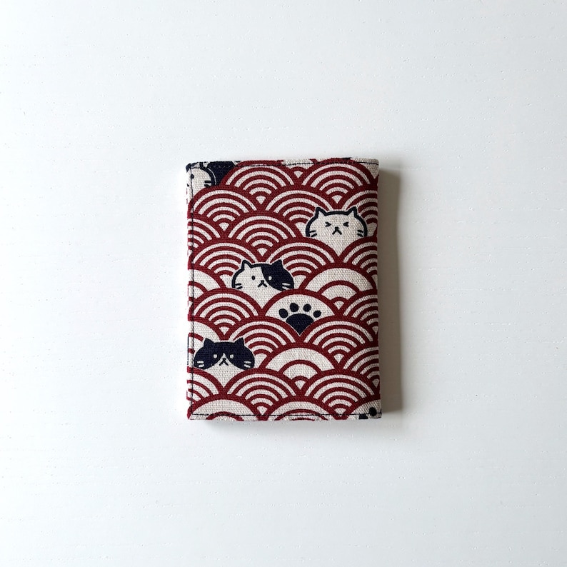 May include: A red and white fabric wallet with a pattern of black and white cats and paw prints. The fabric has a wave-like pattern.