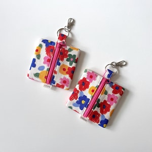 May include: Two small pouches with a floral pattern, pink zips, and key rings. The pouches have a white background with red, pink, blue, yellow, and green flowers. Each pouch has a small tag that reads "RESET".