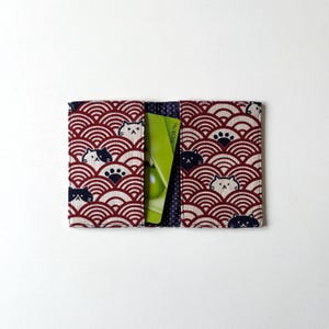 May include: Red and white fabric card holder with a black and white cat pattern. The card holder has a pocket for a credit card or ID card.