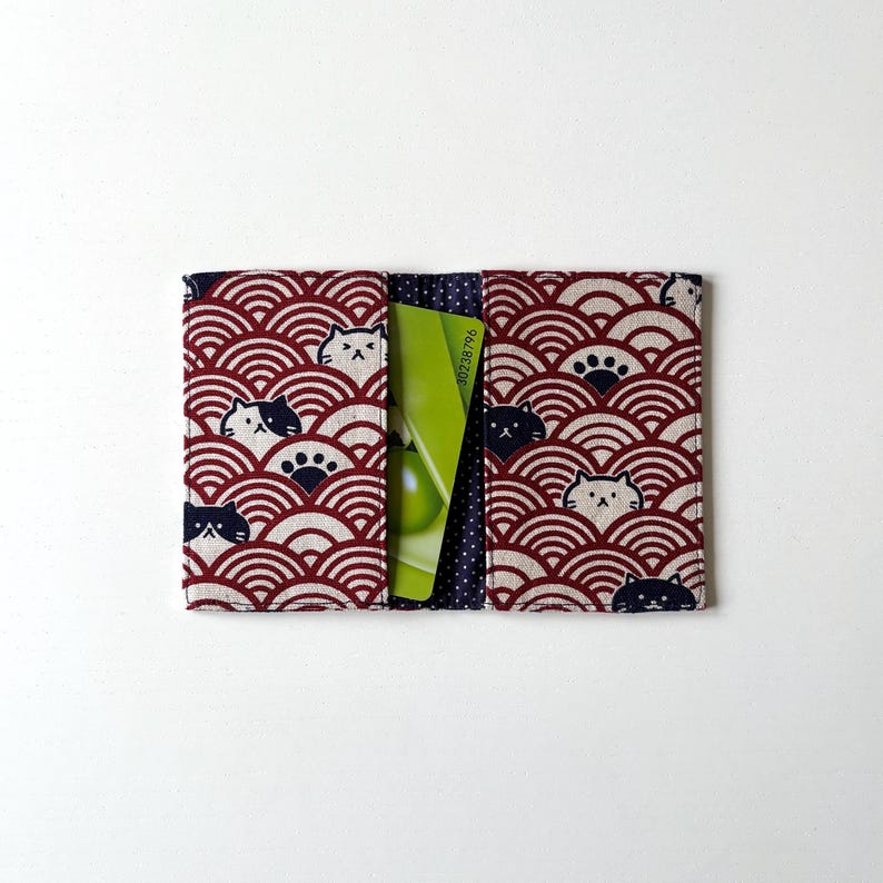May include: Red and white fabric card holder with a black and white cat pattern. The card holder has a pocket for a credit card or ID card.