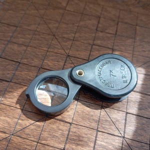 Könnte beinhalten: Eine schwarze Lupe mit 7-facher Vergrößerung. Die Lupe ist aus Kunststoff und hat ein faltbares Design. Der Text "DIAMAG 7x" und "ULTRA 250X" ist auf der Seite aufgedruckt.