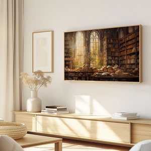 May include: A framed print of a painting depicting a large, sunlit room filled with bookshelves and stacks of books. The room has a large arched window with a view of trees and a bright sky.