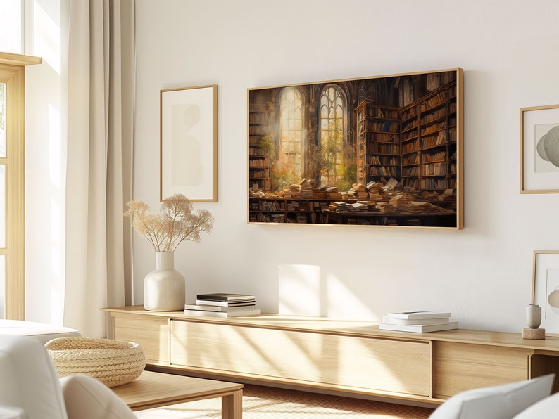 May include: A framed print of a painting depicting a large, sunlit room filled with bookshelves and stacks of books. The room has a large arched window with a view of trees and a bright sky.