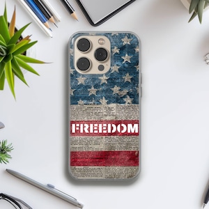 May include: Clear phone case featuring a design inspired by the American flag. The top portion displays a blue field with white stars, while the bottom has red and white stripes with the word "FREEDOM" in bold white letters. The case is designed to fit a smartphone.