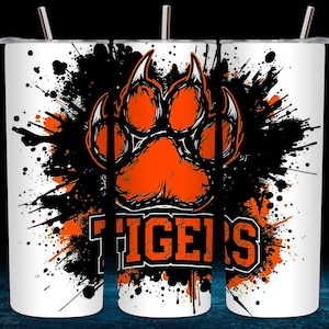 May include: White tumbler with an orange tiger paw print and the word "TIGERS" in orange and black. The design includes black and orange paint splatters. The tumbler has a silver straw.