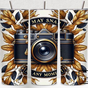 May include: A white tumbler with a gold and black vintage camera design. The camera has a lens with a gold rim and the text "I May Snap Any Moment" is printed on the tumbler.