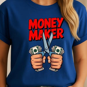 May include: A blue t-shirt with the words "MONEY MAKER" in red, outlined in black. The graphic shows hands holding stacks of money, with scissors cutting through the center. The scissors are blue.