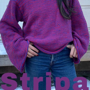 Può includere: Un maglione a righe con righe rosse e blu. Il maglione ha maniche lunghe e un collo rotondo. Il maglione è indossato da una persona che indossa jeans blu.