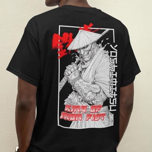 May include: Black t-shirt with a white graphic of a samurai warrior wearing a straw hat and holding a sword. The text "KING OF IRON FIST" and Japanese characters are printed on the shirt.