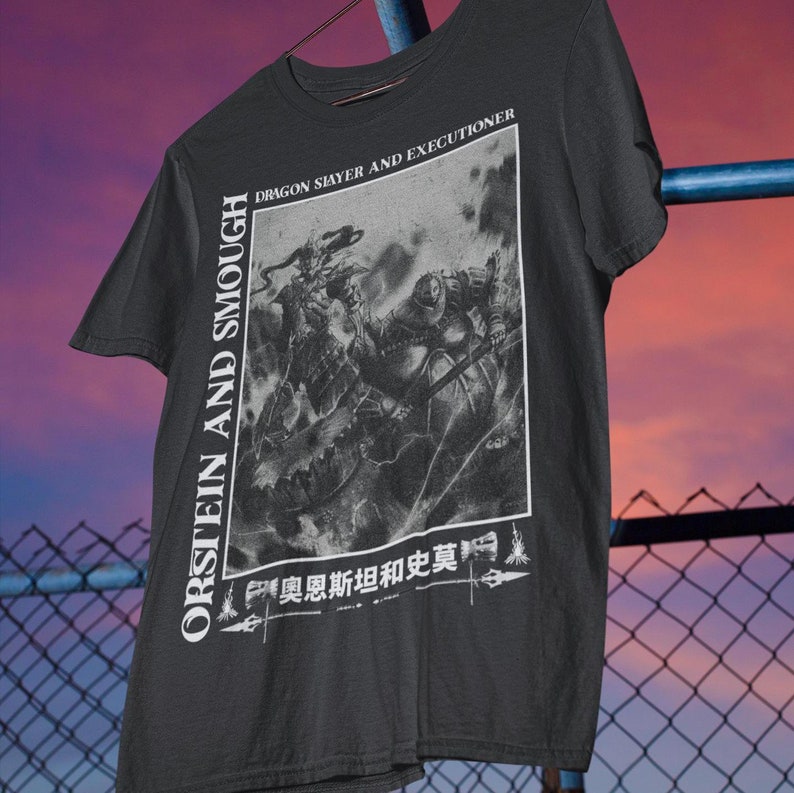 May include: Dark grey t-shirt with a monochrome graphic depicting a battle between a dragon and a knight. The shirt displays the text "ORSTEIN AND SMOUGH" vertically and "DRAGON SLAYER AND EXECUTIONER".
