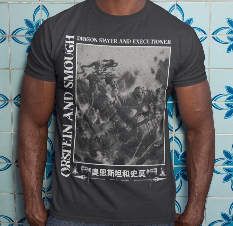 May include: Dark grey t-shirt with a black and white graphic depicting a battle scene, with the text "DRAGON SLAYER AND EXECUTIONER." The shirt also features the text "ORSTEIN AND SMOUGH" vertically and Japanese text at the bottom.