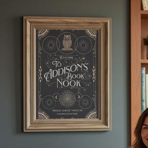 May include: A framed sign reading "Welcome to Addison's Book Nook" is on a grey wall. A woman in a grey jumper and blue jeans sits in a white armchair. A bookshelf with books is visible in the background.