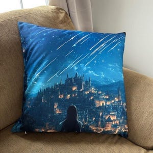 Könnte beinhalten: Ein blaues Kissen mit einem gedruckten Bild einer Stadtlandschaft bei Nacht mit Sternschnuppen am Himmel. Eine einsame Figur steht im Vordergrund und blickt auf die Stadt.