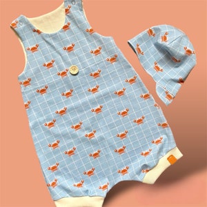 Può includere: Un body per neonato di colore azzurro chiaro con bordino bianco e un motivo di granchi arancioni. Viene fornito con un cappello abbinato di colore azzurro chiaro con bordino bianco e un motivo di granchi arancioni.