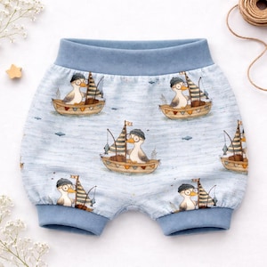 Könnte beinhalten: Hellblaue Baby-Shorts mit einem sich wiederholenden Muster von Cartoon-Enten in Segelbooten. Die Enten tragen Hüte und Brillen, und die Boote haben Segel und Angelruten. Der Bund und die Bündchen sind einfarbig hellblau.
