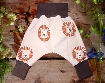 Könnte beinhalten: Weiße Babyhose mit braunem Bund und Bündchen. Die Hose hat ein Löwenkopf-Muster.