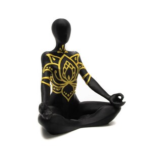 May include: Black figurine of a person sitting in a yoga pose with gold painted lotus flower design on the chest.