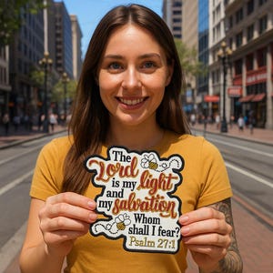 May include: A patch with the text "The Lord is my light and my salvation. Whom shall I fear? Psalm 27:1" in a decorative font, with bee illustrations. The patch has a black border and is held by a person wearing a yellow shirt.