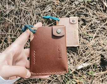 Peut inclure: Deux portefeuilles en cuir marron avec un cordon bleu. Le portefeuille de gauche porte le mot "FINCH" en relief. Le portefeuille de droite porte le mot "FINCH" en relief.