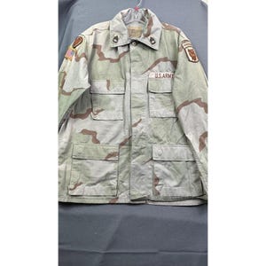 May include: A desert camouflage military jacket with the words "U.S. ARMY" printed on the front. The jacket has multiple pockets, patches, and a collar. The color scheme includes tan, brown, and green.