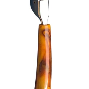 May include: A silver knife sharpener with a brown and orange marbled plastic handle.