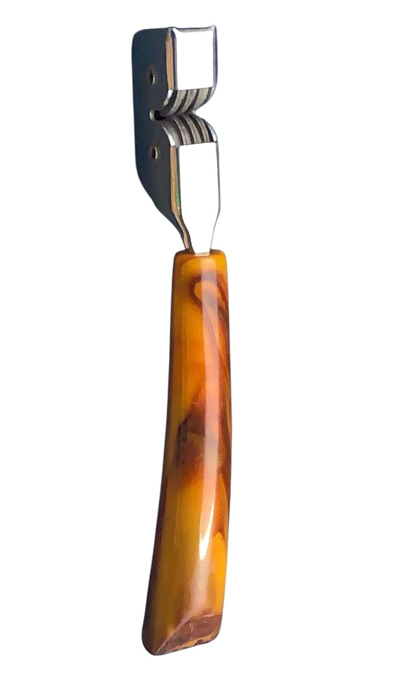 May include: A silver knife sharpener with a brown and orange marbled plastic handle.
