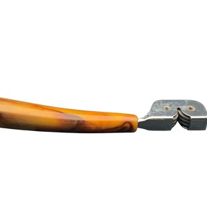 May include: A vintage knife sharpener with a brown and yellow marbled plastic handle and a silver metal sharpening mechanism.