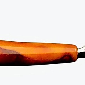 May include: A vintage glass cutter with a brown and orange marbled plastic handle. The cutter has a metal blade and a white plastic base.