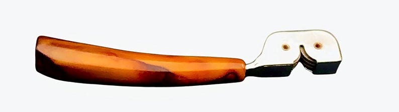 May include: A vintage glass cutter with a brown and orange marbled plastic handle. The cutter has a metal blade and a white plastic base.