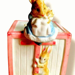 May include: A white ceramic mug with a black handle and the text "But First, Coffee" in a bold, black font. The mug is set against a blurred background, suggesting a cozy setting.