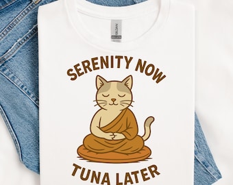 May include: White t-shirt with a cartoon cat meditating in a lotus position. The cat is wearing a brown robe and sitting on a brown cushion. The text "SERENITY NOW" is above the cat, and "TUNA LATER" is below.