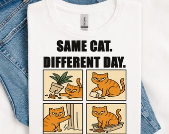 Puede incluir: Camiseta blanca con el texto "SAME CAT. DIFFERENT DAY." y una historieta de cuatro paneles de un gato naranja. El gato se representa causando travesuras, como derribar una planta.