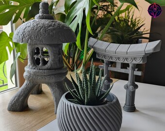 May include: Three gray concrete decorative items: a small pagoda-style structure, a torii gate, and a planter with a succulent plant. The items are arranged on a wooden surface.