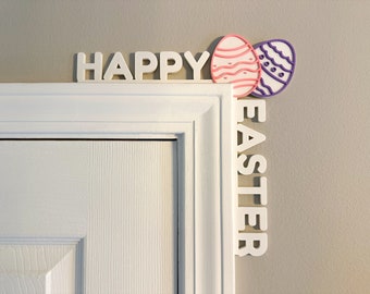 May include: White wooden letters spelling "Happy Easter" with two pink and purple Easter eggs on a white door frame.