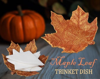 May include: A gold-painted maple leaf trinket dish with a textured surface. The dish is filled with white paper napkins. The text "Maple Leaf Trinket Dish" is written below the dish.