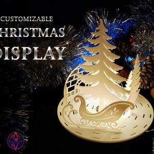 May include: White customizable Christmas display featuring a stylised tree, a sleigh, and a snowflake design. The display is lit with warm white lights.
