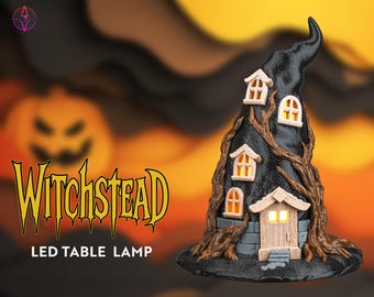 May include: A black witch hat-shaped LED table lamp with a house design. The lamp features a textured surface, small windows, and a wooden door. The text "Witchstead" is displayed in yellow.