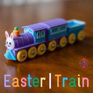 May include: A colorful toy train with an Easter theme. The train is primarily purple and teal, with yellow wheels. The front of the train features a bunny face with a carrot on top. The text "Easter | Train" is displayed below the train.