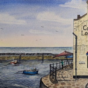 May include: Watercolour painting of a coastal scene with a building displaying "Cod & Lobster". A blue boat is in the water near a stone pier. A red and blue umbrella shades a small patio. The sky is blue with a few birds.