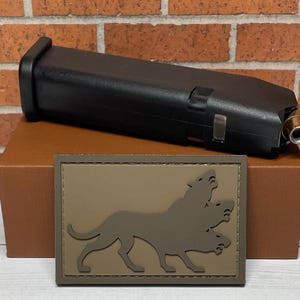 May include: A brown leather box with a black magazine inside. The box has a brown patch with a three-headed dog silhouette.