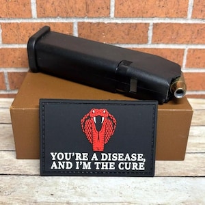 May include: Black tactical patch with a red cobra and the text "You're a disease, and I'm the cure".