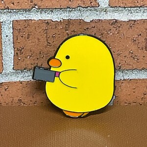 May include: A yellow cartoon chick holding a black and pink cell phone. The chick has black eyes and a pink beak.