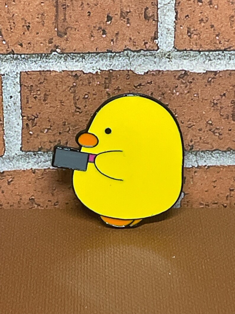 May include: A yellow cartoon chick holding a black and pink cell phone. The chick has black eyes and a pink beak.