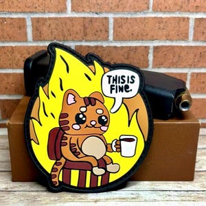 May include: A yellow and orange cartoon cat sits in a chair with a cup of coffee in a fire. The cat is smiling and says "This is fine."